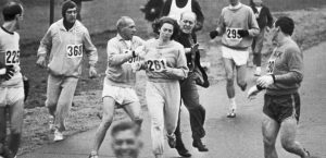 Trainer Jock Semple -- in street clothes -- enters the field of runners (left) to try to pull Kathy Switzer (261) out of the race. Male runners move in to form a protective curtain around female track hopeful until the protesting trainer is finally wedged out of the race
